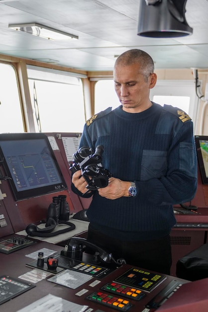 Wachoffizier mit Fernglas auf der Navigationsbrücke. Kaukasischer Mann im blauen Uniformpullover auf der Brücke eines Frachtschiffs