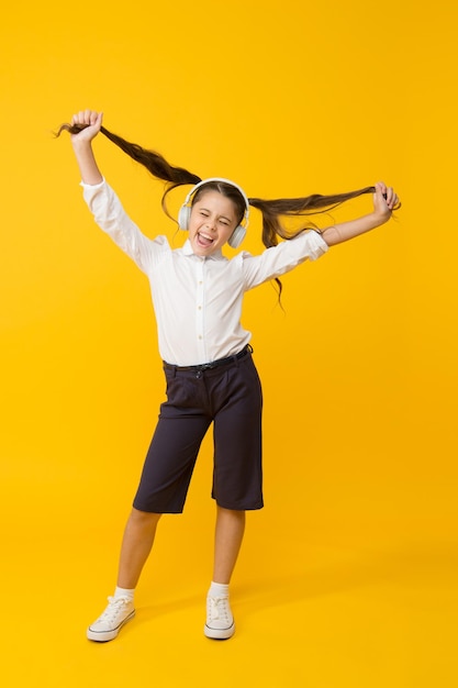 Wachsen Sie Haare mit Musik Kleines Kind trägt lange Schwanzfrisur und Kopfhörer für die Schule Kleines Mädchen, das Frisur auf gelbem Hintergrund hält Nettes Kind, das Musik und ihre Frisur genießt Einfache Frisur