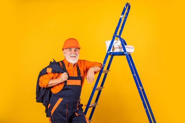 Wärmedämmung arbeitet Maler Mann Treppe Reparaturen durchzuführen Mann in Arbeitskleidung Malerei Wand in leerem Raum Maler in Overall und Mütze mit Farbeimer Bauarbeiter Fassade malen