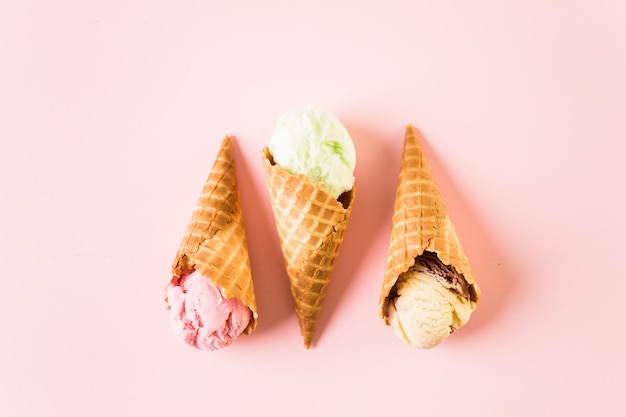 Waffel-Eistüten mit Teller mit Eiskugeln auf rosa Hintergrund.