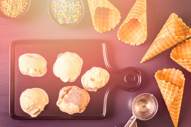 Waffel-Eistüten mit Teller mit Eisportionierern auf einem schwarzen Schneidebrett.