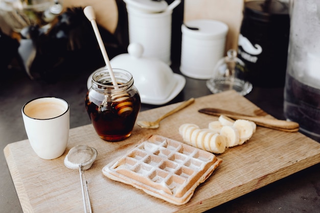 Waffel und Scheiben der Banane auf einem hölzernen Behälter nahe bei einem Honigglas