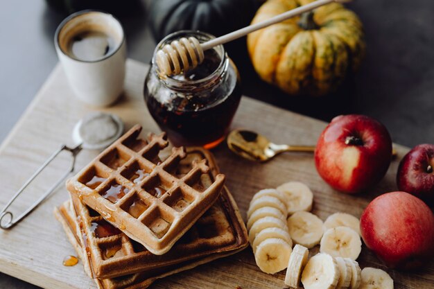 Waffel und Scheiben der Banane auf einem hölzernen Behälter nahe bei einem Honigglas