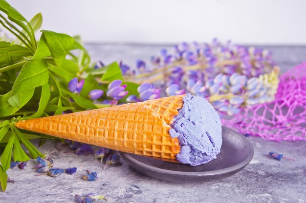 Waffelkegel mit purpurroter lila Eiscreme auf dem dunkelgrauen Hintergrund Lupinen verzierend