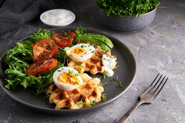 Waffeln, Kräuter, Tomaten, Salat, Eier und Gewürze auf einem Teller serviert