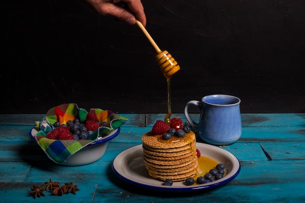 Waffeln mit Blaubeeren und Himbeeren mit etwas Honig zum Frühstück auf blauem hölzernem Hintergrund