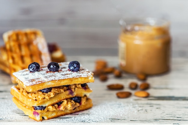 Waffeln mit Erdnussbutter und Heidelbeerbeeren auf hellem Holztisch. Nahaufnahme, selektiver Fokus