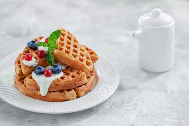 Waffeln mit Heidelbeeren und Johannisbeeren gegossen mit Joghurt auf einem weißen Porzellanteller Vorderansicht