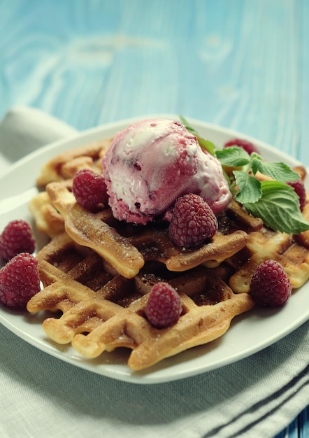 Waffeln mit Himbeereis und frischen Himbeeren, dekoriert mit Minze auf blauem Holzhintergrund