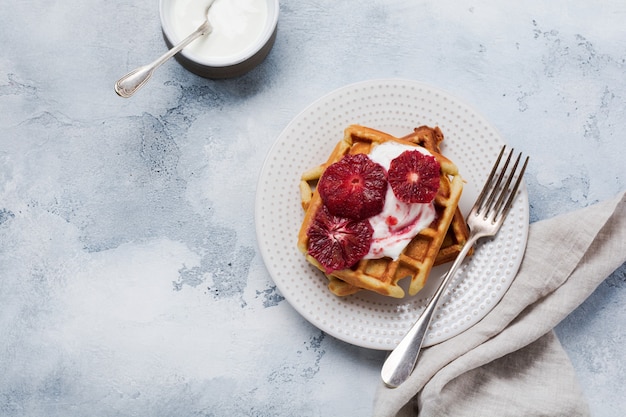 Waffeln mit Joghurtsaucen und roten sizilianischen Orangensaucen auf heller alter Oberfläche. Draufsicht.