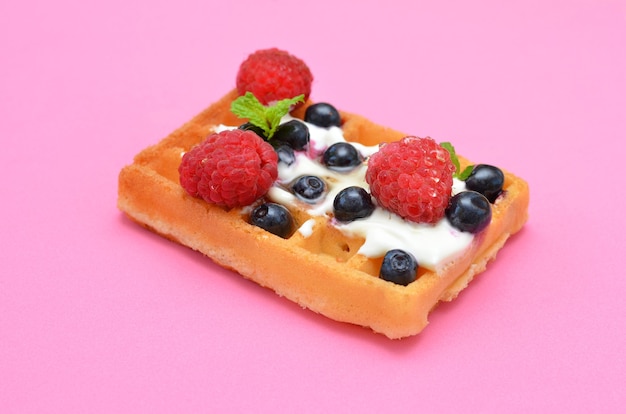 Waffeln mit Sahne und Beeren auf rosa Hintergrundnahaufnahme