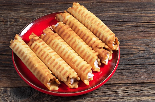 Waffelröllchen mit Sahne in roter Platte auf altem Holztisch. Hausgemachtes Backen