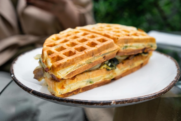 Waffelsandwich mit Spinat, Pilzen und Käse auf einem Teller im Freien in einem Straßencafé, Nahaufnahme, weicher Fokus