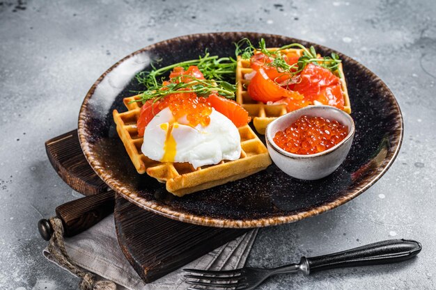 Waffle belga com cream cheese, rodelas de salmão, ovo e caviar vermelho. plano de fundo cinza. vista do topo.