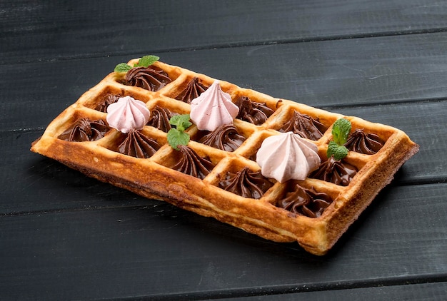 Waffle belga com merengue e creme de chocolate em um fundo escuro de madeira
