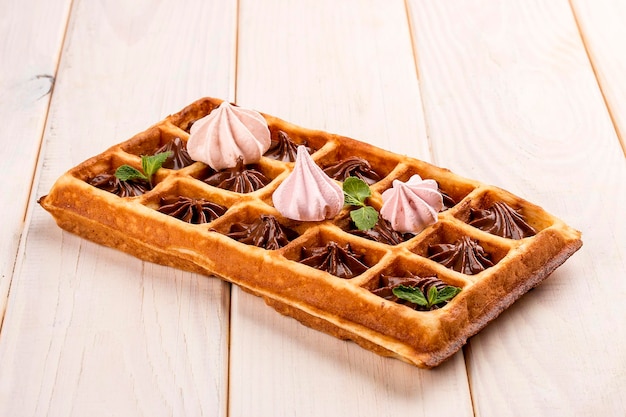 Waffle belga com merengue e creme de chocolate Sobre um fundo claro de madeira