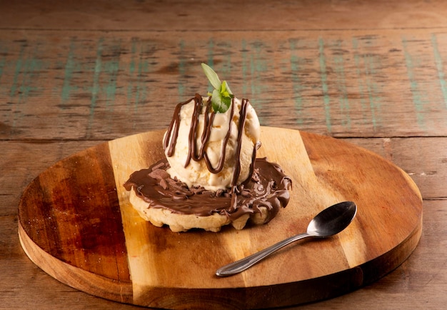 Waffle com creme de chocolate e avelã e uma bola de sorvete de baunilha na tábua redonda de madeira com sobremesa de café de colher
