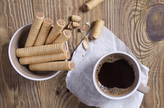 Waffle de chocolate rola em uma tigela e quebrado perto e uma xícara de café na vista de cima da mesa de madeira