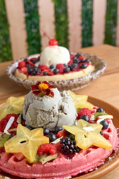 Waffle de sorvete rosa delicioso com frutas vermelhas e carambola na mesa de madeira