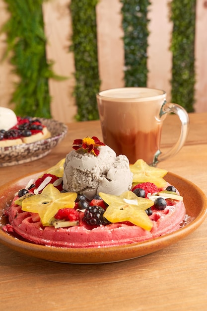 Waffle de sorvete rosa delicioso com frutas vermelhas e carambola na mesa de madeira