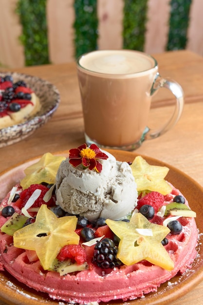 Waffle de sorvete rosa delicioso com frutas vermelhas e carambola na mesa de madeira