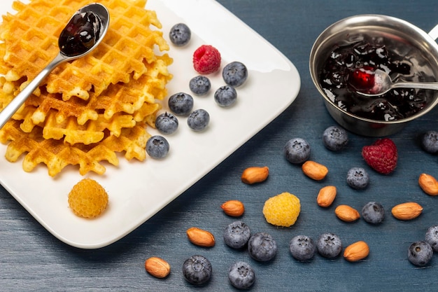 Waffles bayas y cuchara con mermelada en plato blanco Nueces y bayas en la mesa