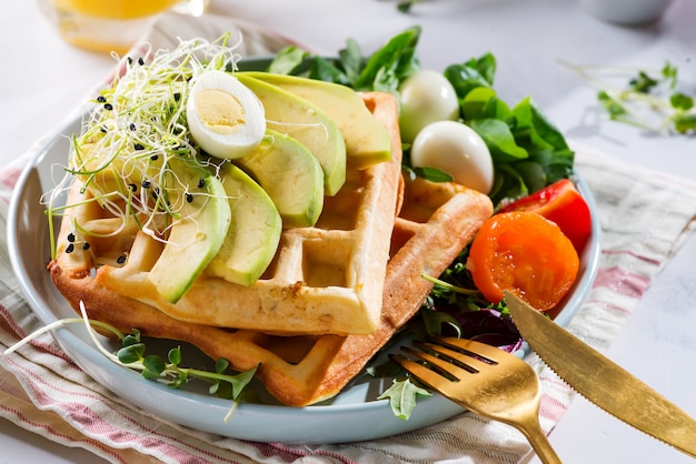 Waffles belgas con aguacate, huevos, microverde y tomates con jugo de naranja sobre mesa de mármol