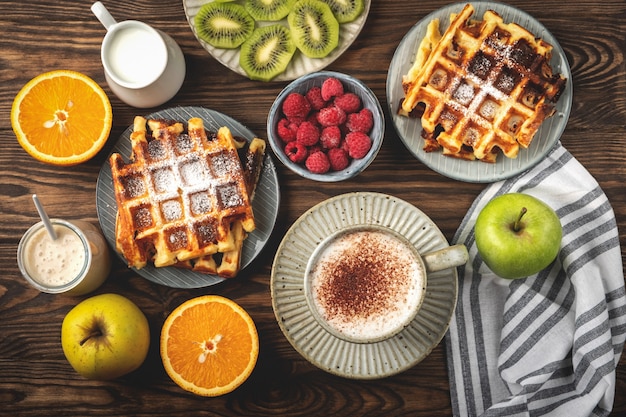 Waffles belgas, café, iogurte, frutas e bagas em um fundo de madeira, conceito de café da manhã.