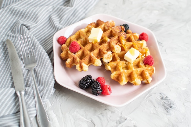 Waffles Belgas caseiros com manteiga Mel Bagas Framboesas Amoras Mesa Toalha de cozinha Prato rosa Café da manhã