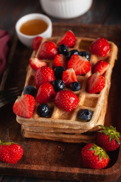 Waffles belgas caseiros frescos numa velha mesa de madeira com framboesas, mirtilos e mel.