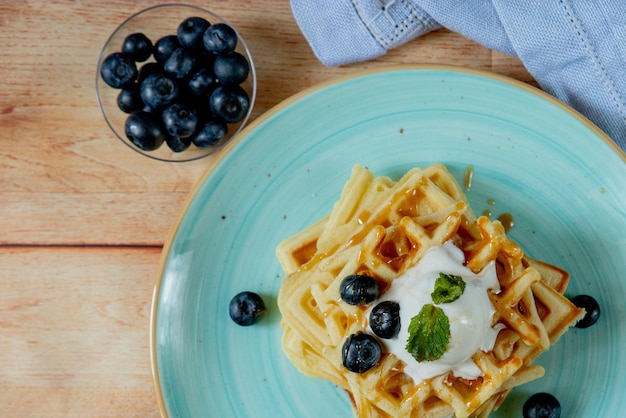 Waffles belgas clássicos caseiros frescos cobertos com sorvete de mirtilos frescos e hortelã em fundo de madeira vista de cima para baixo Waffles salgados Conceito de café da manhã