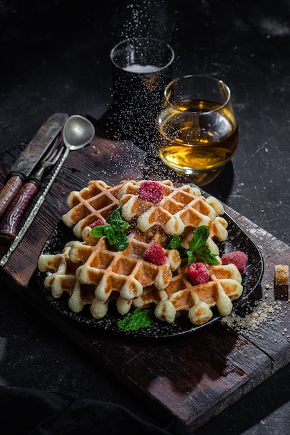 Waffles belgas com framboesas e hortelã num prato escuro