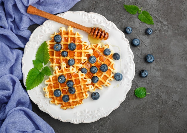 Waffles belgas com mel e frutas frescas, mirtilo e hortelã na superfície preta, deliciosa sobremesa