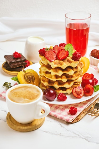 Waffles belgas com morangos, damascos, cerejas, suco e uma xícara de café preto