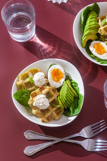 Waffles belgas com ovo de queijo cremoso e abacate em um prato branco café da manhã saudável