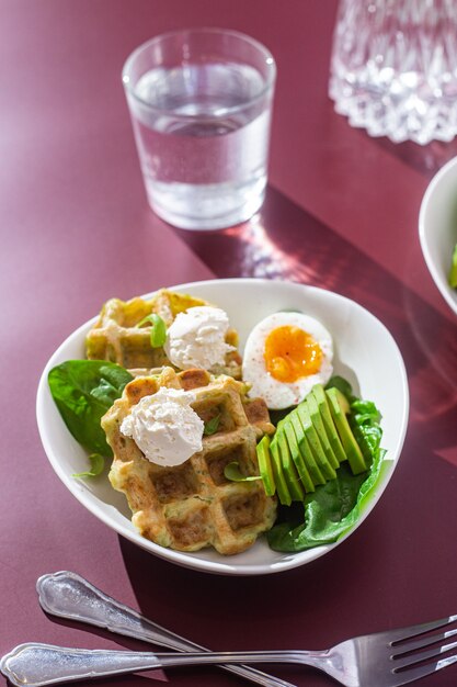 Waffles belgas com ovo de queijo cremoso e abacate em um prato branco Café da manhã saudável