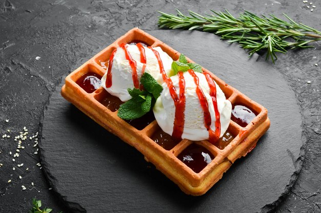 Waffles belgas: com sorvete, geleia de morango e hortelã. Sobremesa. Em uma placa de pedra preta.