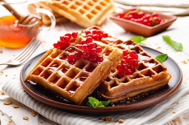 Waffles belgas crujientes caseros servidos con grosella roja y miel