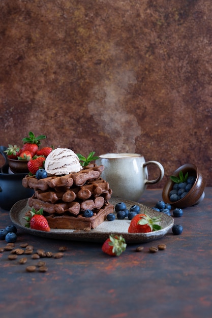 Waffles belgas de chocolate com frutas frescas e sorvete de café em uma placa de cerâmica na mesa marrom