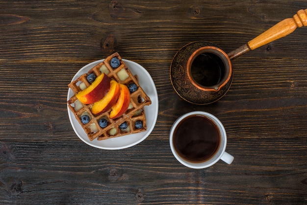 Waffles belgas de chocolate com frutas, xícara de café e cezve em madeira. Delicioso café da manhã. Vista do topo