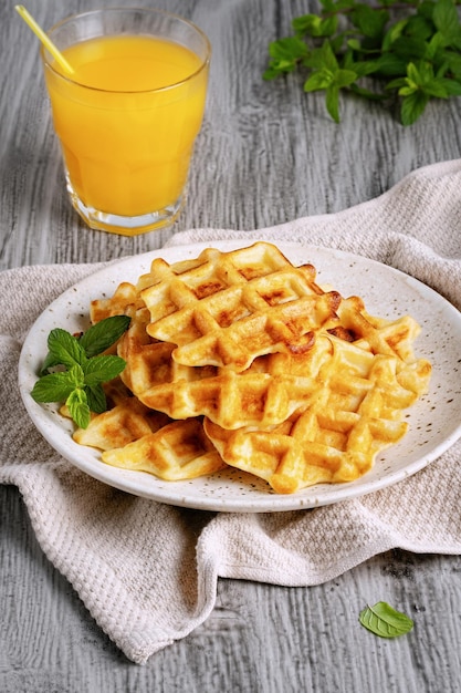 Waffles belgas e suco de laranja em um fundo cinza