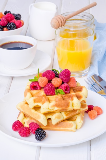 Waffles belgas con frambuesas frescas y moras en un plato blanco para el desayuno