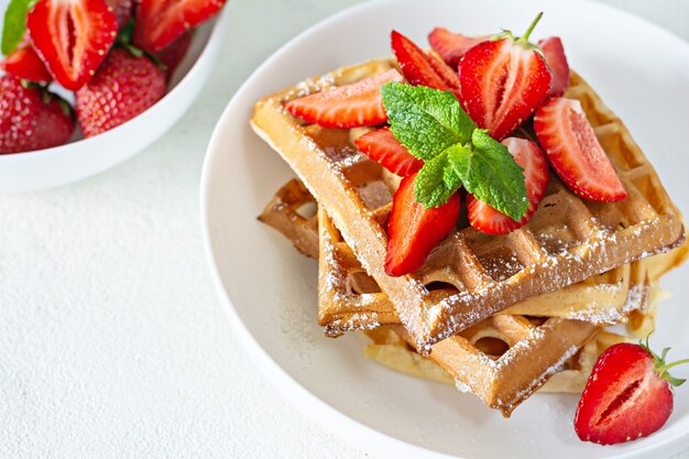 Waffles belgas frescos y crujientes con fresas maduras, menta y miel para el desayuno