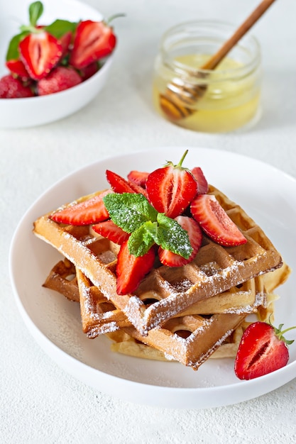 Waffles belgas frescos y crujientes con fresas maduras, menta y miel para el desayuno