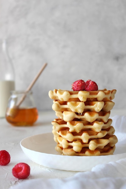 Waffles belgas no prato branco servidos com framboesas framboesas de mel com leite engarrafado no fundo