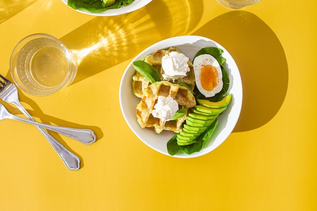 Waffles belgas con queso crema, huevo y aguacate en un plato blanco Desayuno saludable