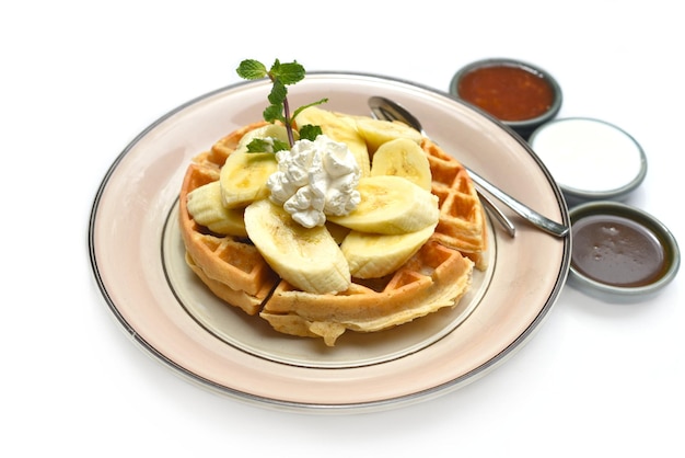 Waffles belgas con rodajas de plátano y helado en un plato con cobertura de chocolate y salsa de frutas