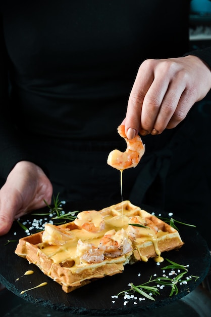 Waffles belgas sanduíche com molho de camarão e queijo em um prato nas mãos de um chef em um fundo preto