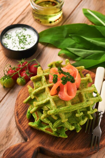 Waffles belgas verdes Espinafre ou alho selvagem ou waffles pesto com salmão vermelho e molho de creme na chapa preta sobre fundo escuro de madeira rústica Brunch delicioso café da manhã lanche Mock up