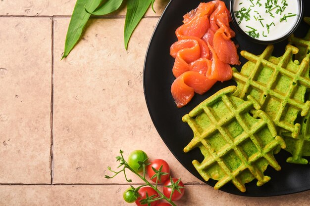 Waffles belgas verdes Espinafre ou alho selvagem ou waffles pesto com salmão vermelho e molho de creme no antigo fundo da mesa de azulejos bege Delicioso café da manhã lanche na vista superior de fundo escuro